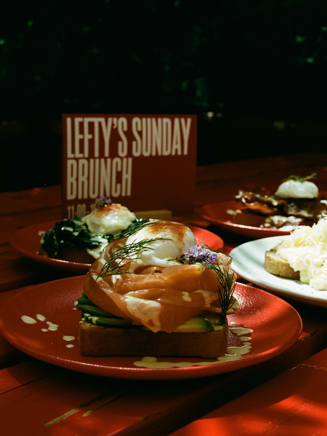 Sunday brunch on the red tables: salmon and poached-egg toasts on red plates beside a printed LEFTY'S SUNDAY BRUNCH card.