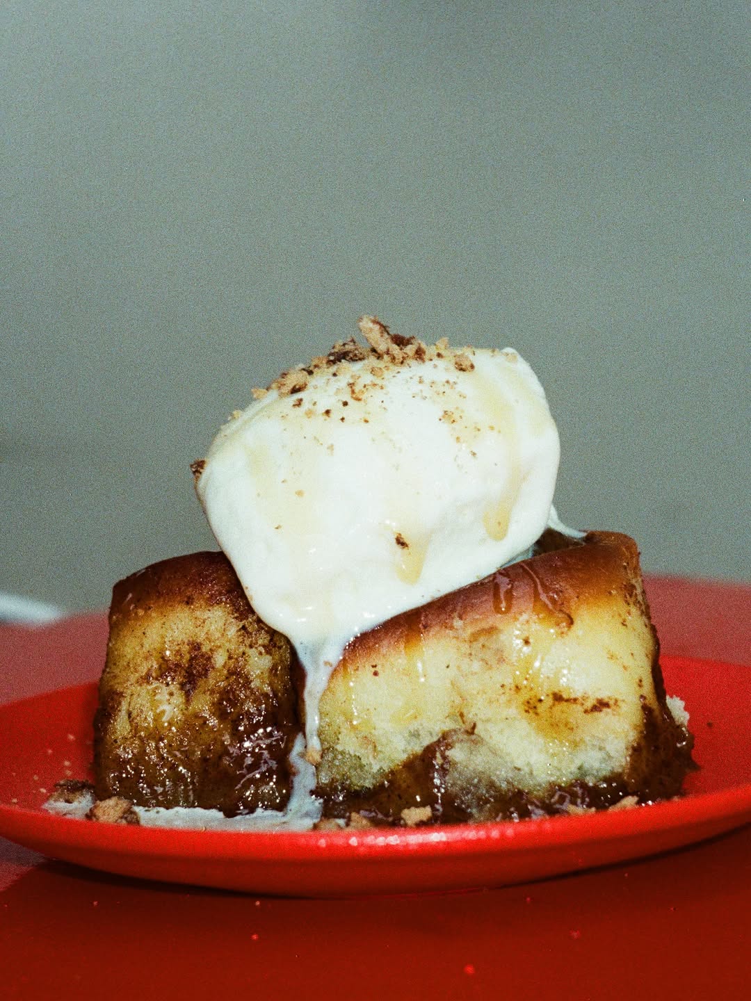 Cinnamon-dusted rolls on a red plate, a scoop of ice cream melting over them, caramel underneath.