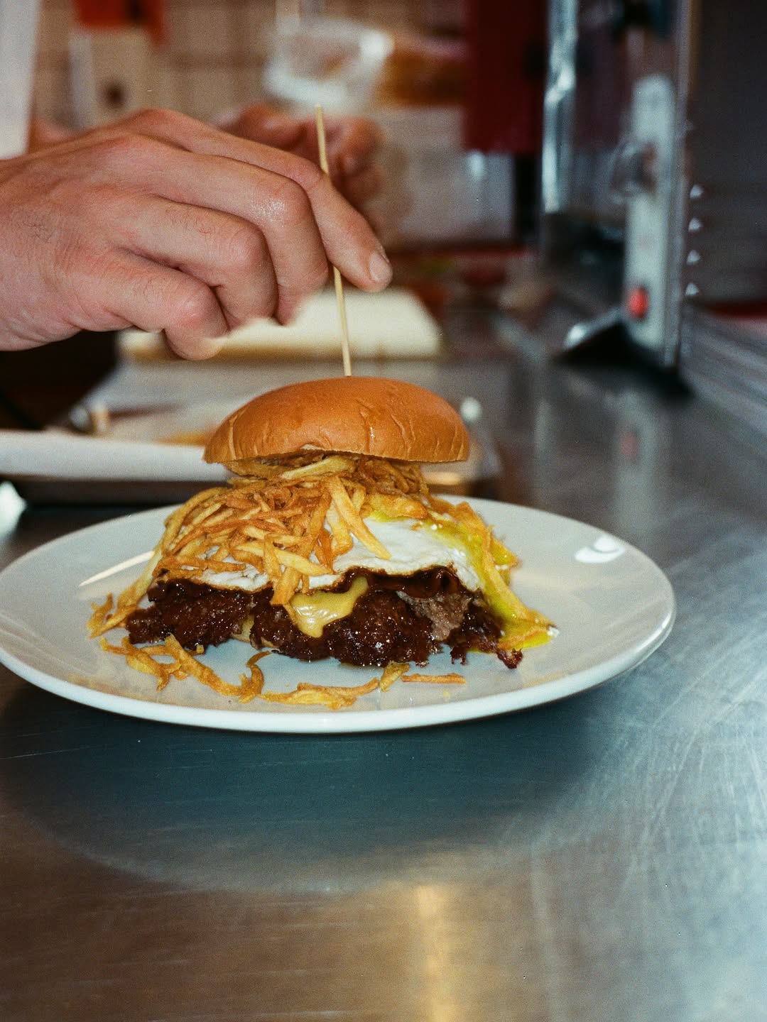 The Hangover Burger on a white plate at the counter: smashed patties, melted cheese, a fried egg and a pile of crunchy potatoes under the bun.